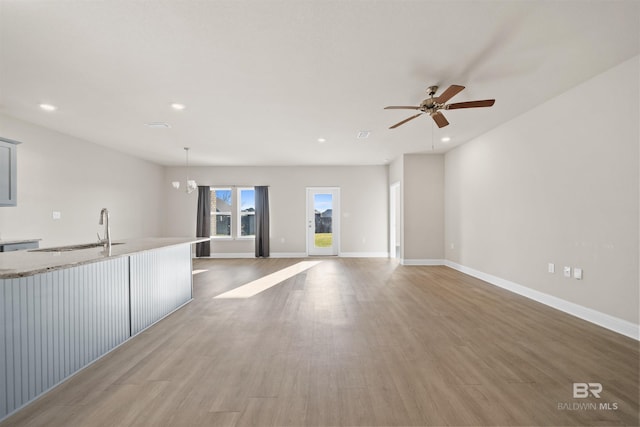 unfurnished living room with recessed lighting, baseboards, a sink, and wood finished floors