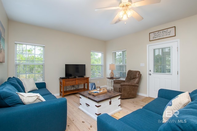 living area with baseboards, light wood-type flooring, a ceiling fan, and a healthy amount of sunlight