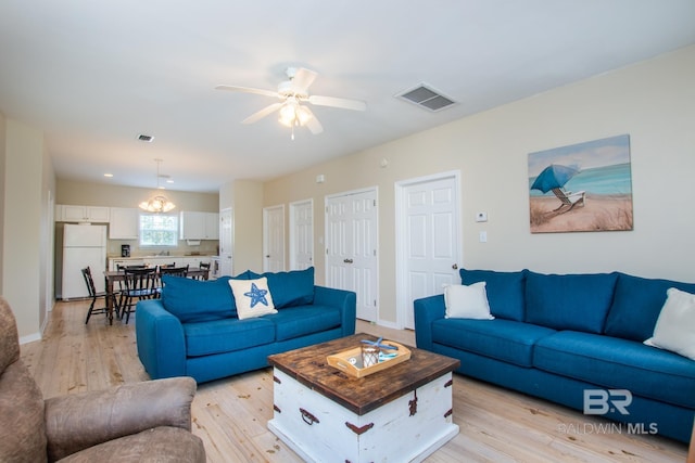 living room with ceiling fan with notable chandelier, light wood-style flooring, visible vents, and baseboards