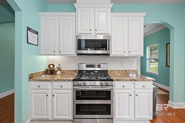 2554 Masters Ct, Mobile, AL 36618 - kitchen featuring stainless steel appliances, arched walkways, tasteful backsplash, wood finished floors, and white cabinetry