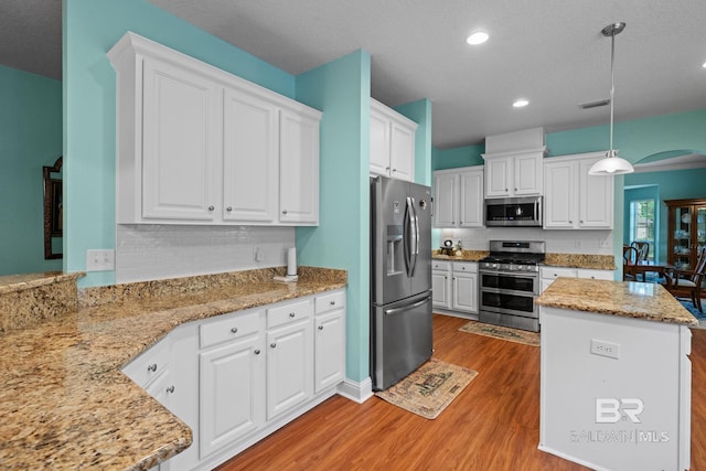 2554 Masters Ct, Mobile, AL 36618 - kitchen featuring appliances with stainless steel finishes, light wood-style floors, arched walkways, white cabinets, and decorative light fixtures