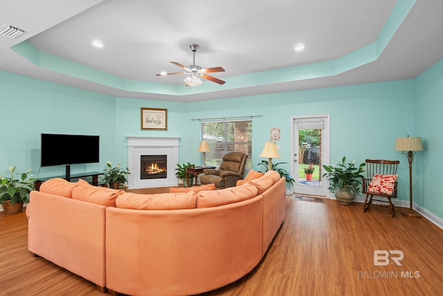 2554 Masters Ct, Mobile, AL 36618 - living area with a tray ceiling, wood finished floors, a glass covered fireplace, ceiling fan, and recessed lighting