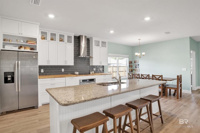 kitchen with wall chimney exhaust hood, appliances with stainless steel finishes, sink, and a center island with sink