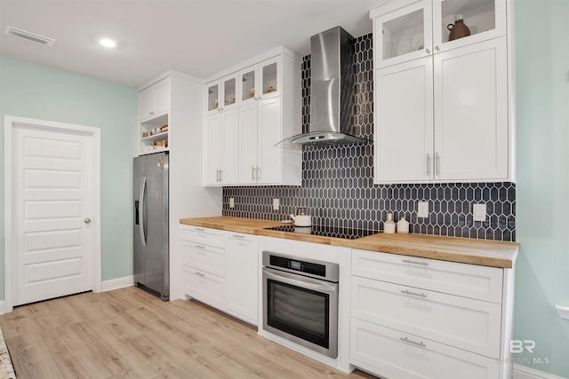 kitchen with white cabinetry, appliances with stainless steel finishes, wall chimney range hood, and wood counters