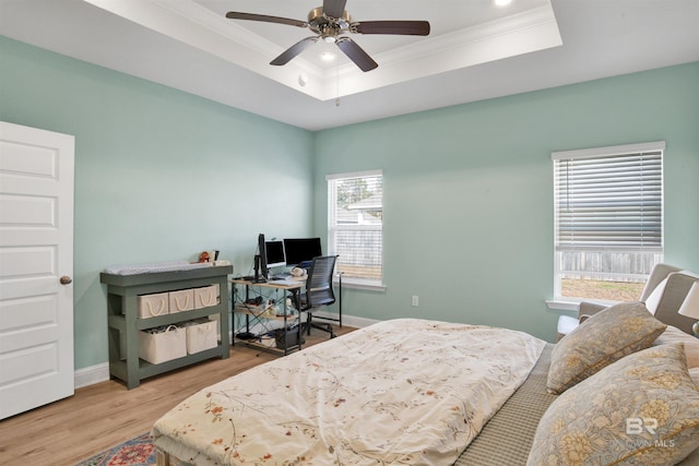 bedroom with ceiling fan, ornamental molding, a raised ceiling, and light hardwood / wood-style floors