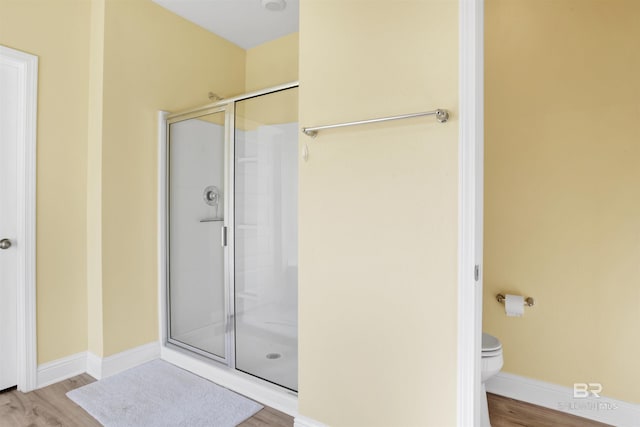 bathroom with toilet, a shower with shower door, and hardwood / wood-style floors