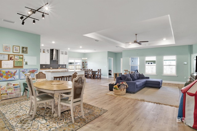 dining area with a tray ceiling, light hardwood / wood-style flooring, a wealth of natural light, and ceiling fan with notable chandelier