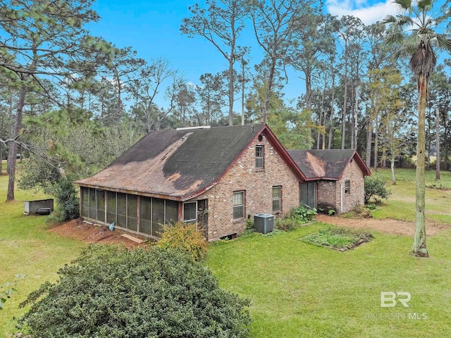 rear view of property with central air condition unit, a sunroom, and a yard