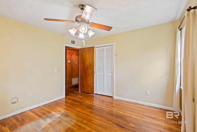 unfurnished bedroom featuring wood-type flooring, a textured ceiling, a closet, and ceiling fan