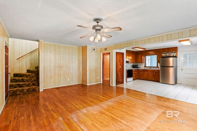 unfurnished living room featuring ceiling fan, wooden walls, a textured ceiling, and light wood-type flooring