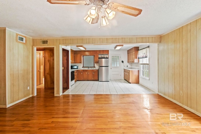 kitchen featuring stainless steel fridge, a textured ceiling, ceiling fan, light hardwood / wood-style floors, and wood walls