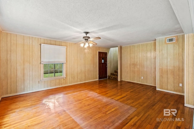 spare room featuring wood-type flooring, a textured ceiling, ceiling fan, and wood walls