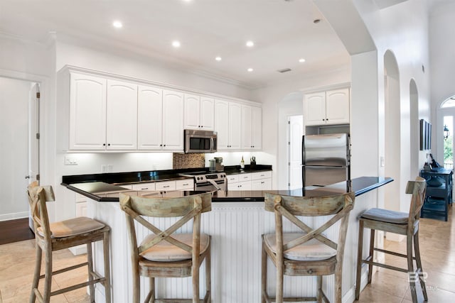 kitchen with kitchen peninsula, white cabinets, a kitchen breakfast bar, ornamental molding, and stainless steel appliances