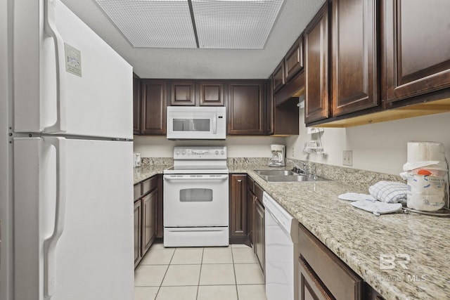 kitchen with light tile patterned flooring, sink, dark brown cabinetry, light stone counters, and white appliances