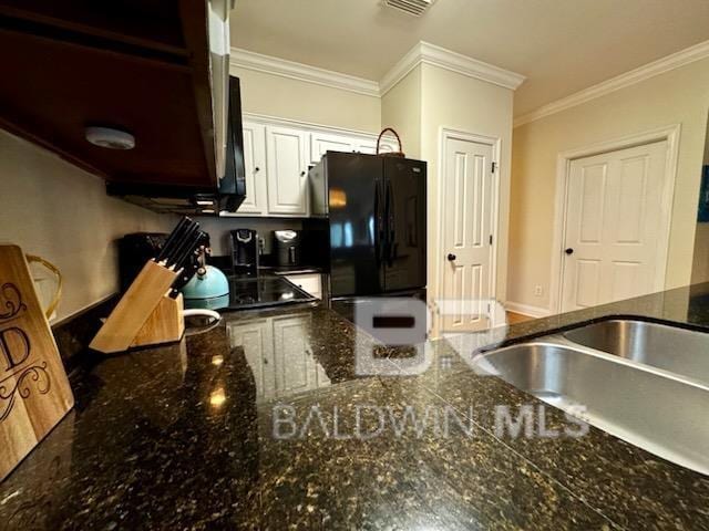 kitchen with white cabinets, black fridge, crown molding, and dark stone counters