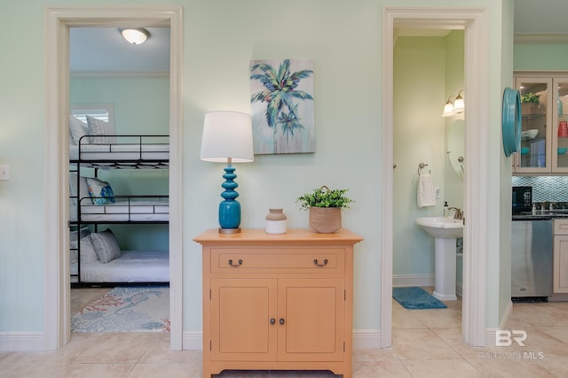 hallway with light tile patterned floors, crown molding, baseboards, and a sink