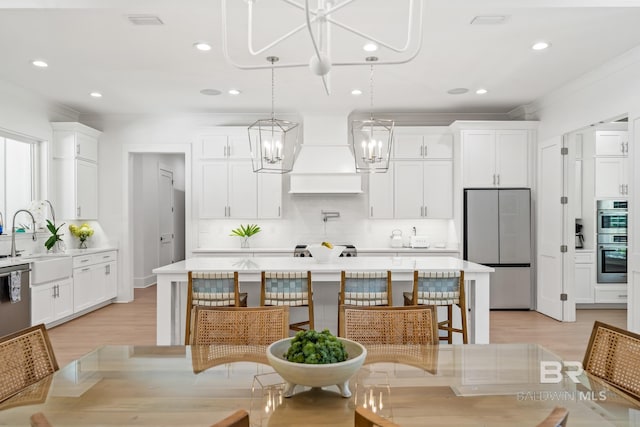 kitchen featuring a sink, white cabinetry, light countertops, appliances with stainless steel finishes, and custom range hood