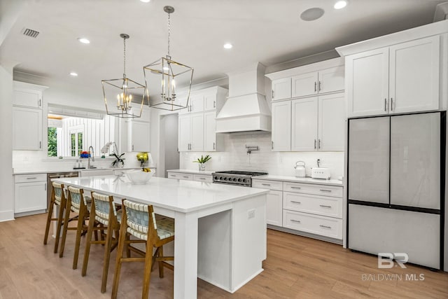 kitchen with visible vents, a kitchen island, stainless steel appliances, light countertops, and premium range hood