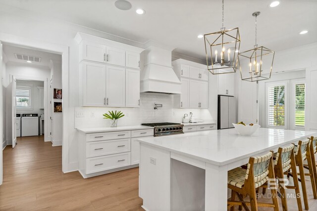 kitchen with a large island, washer and clothes dryer, stainless steel appliances, visible vents, and custom range hood