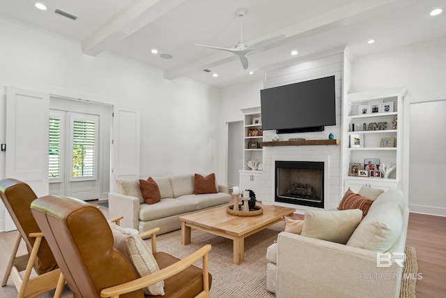 living area featuring a large fireplace, visible vents, ceiling fan, wood finished floors, and beam ceiling