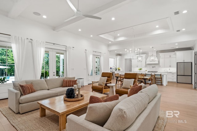 living area featuring light wood-type flooring, french doors, a raised ceiling, and beam ceiling