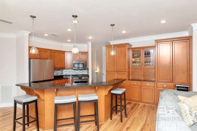 kitchen with stainless steel appliances, hanging light fixtures, a kitchen island with sink, and light wood-type flooring