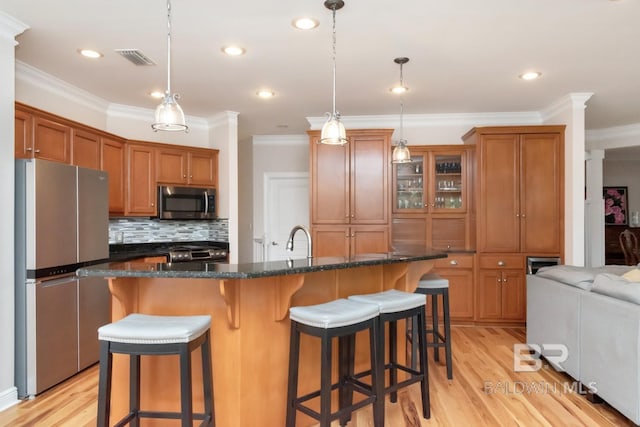 kitchen with stainless steel appliances, light hardwood / wood-style floors, a breakfast bar, decorative light fixtures, and an island with sink