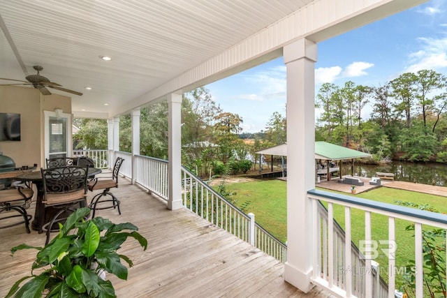 wooden deck with a water view, ceiling fan, and a lawn