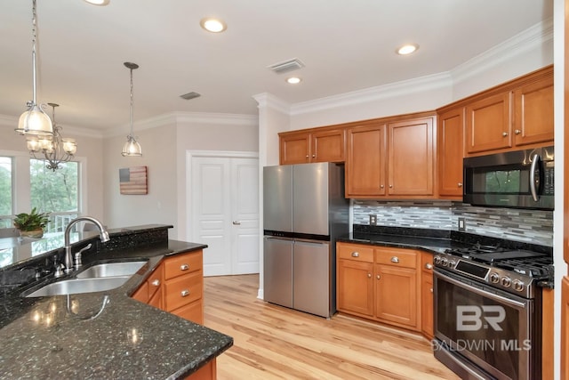 kitchen featuring stainless steel appliances, dark stone counters, hanging light fixtures, sink, and light hardwood / wood-style floors