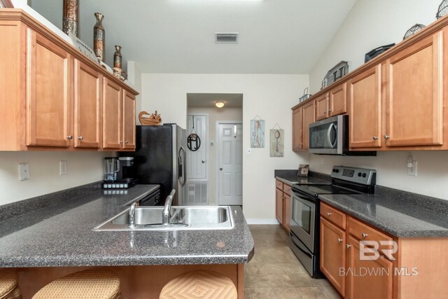 kitchen with appliances with stainless steel finishes, sink, dark stone counters, a kitchen breakfast bar, and light tile patterned flooring