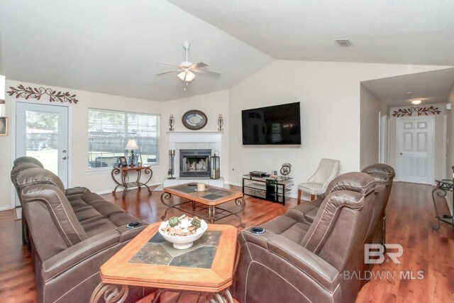 living room featuring ceiling fan, a tiled fireplace, dark wood-type flooring, and lofted ceiling