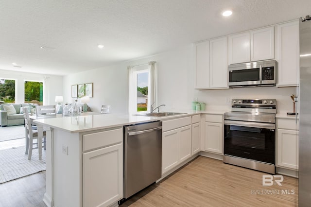 kitchen with a peninsula, a sink, white cabinetry, open floor plan, and appliances with stainless steel finishes