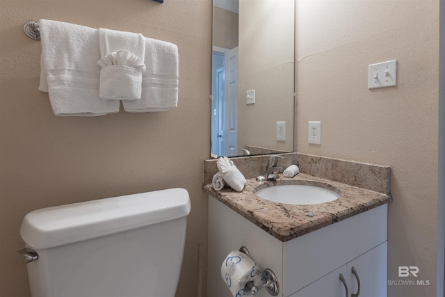 half bath with toilet, vanity, and a textured wall