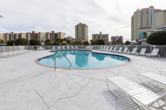 community pool with a patio area, a view of city, and fence