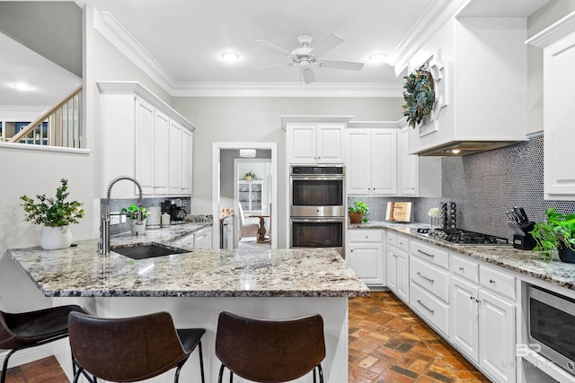 kitchen with light stone counters, tasteful backsplash, white cabinets, appliances with stainless steel finishes, and sink