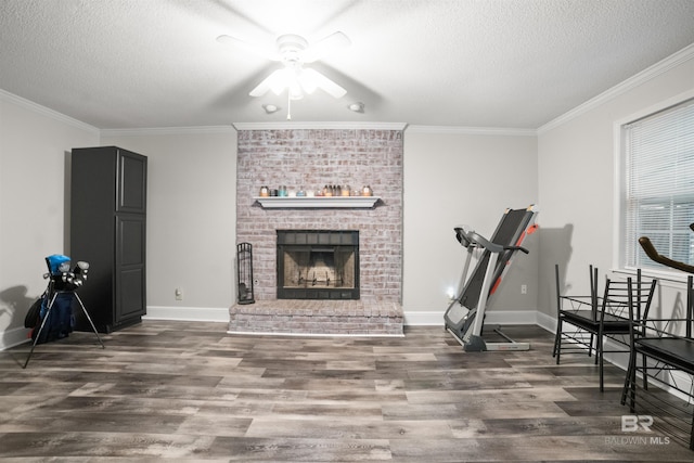 workout room featuring crown molding, dark wood-type flooring, ceiling fan, a fireplace, and a textured ceiling