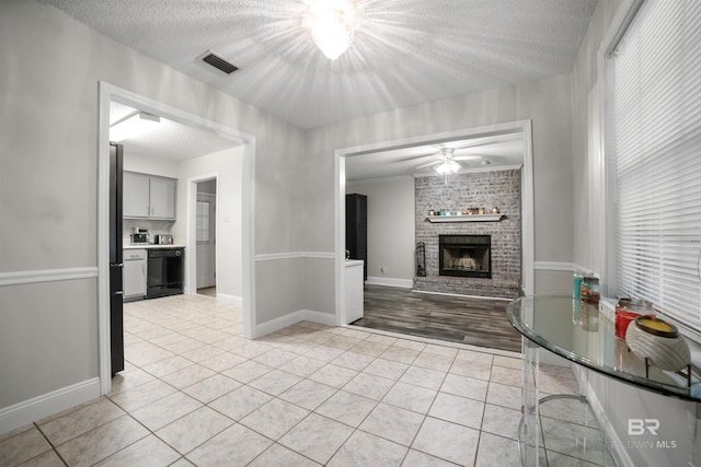 unfurnished living room with light tile patterned flooring, ceiling fan, a textured ceiling, and a fireplace