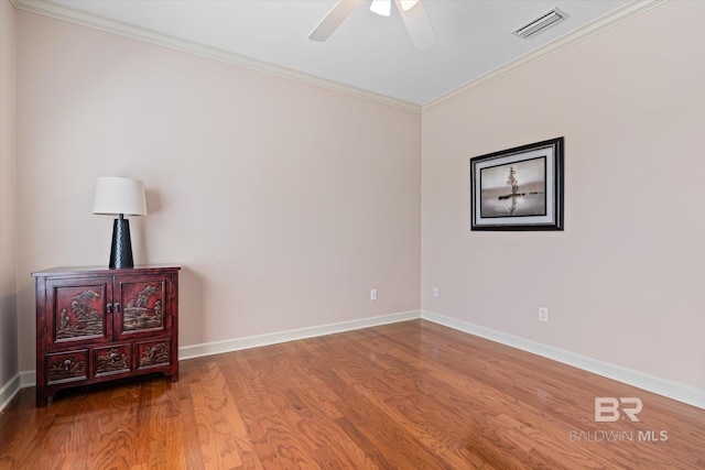 unfurnished room featuring a ceiling fan, wood finished floors, visible vents, baseboards, and crown molding