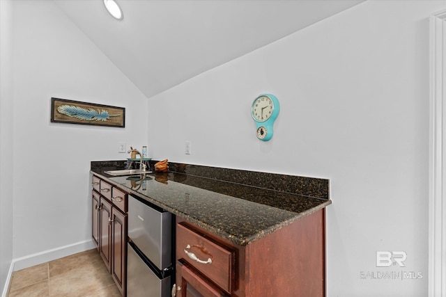 kitchen featuring a sink, freestanding refrigerator, dark stone counters, light tile patterned flooring, and vaulted ceiling