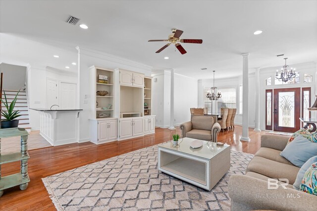 living room featuring light wood-style flooring, decorative columns, ceiling fan with notable chandelier, and visible vents