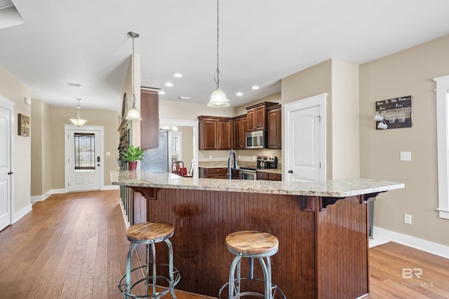 kitchen with light wood-type flooring, light stone counters, a kitchen breakfast bar, appliances with stainless steel finishes, and baseboards