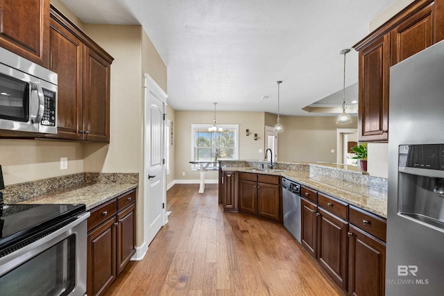 kitchen with light wood-type flooring, pendant lighting, a sink, appliances with stainless steel finishes, and a peninsula