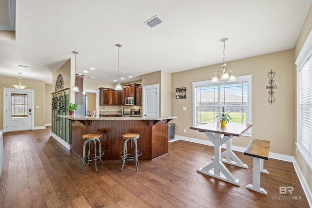 kitchen with dark wood-type flooring, stainless steel microwave, an inviting chandelier, a breakfast bar area, and light stone countertops