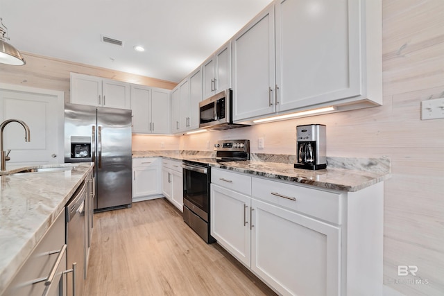 kitchen with appliances with stainless steel finishes, light stone counters, sink, light hardwood / wood-style flooring, and white cabinets