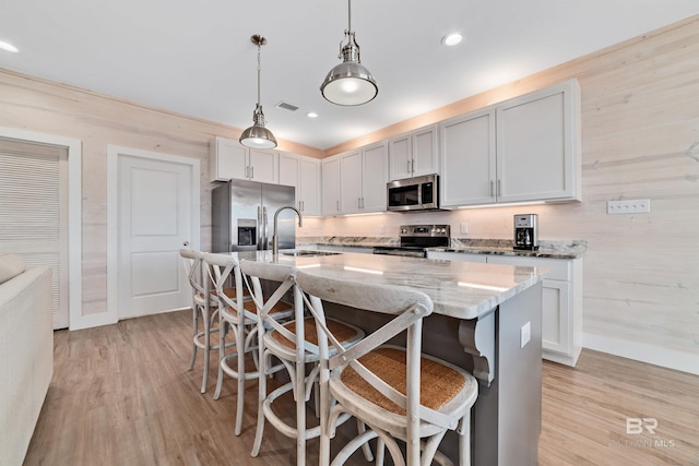 kitchen featuring an island with sink, hanging light fixtures, appliances with stainless steel finishes, and light wood-type flooring