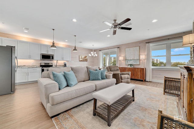 living room with ceiling fan with notable chandelier, sink, and light wood-type flooring