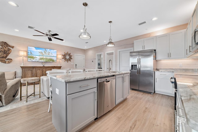 kitchen featuring an island with sink, stainless steel appliances, ceiling fan, and light hardwood / wood-style flooring