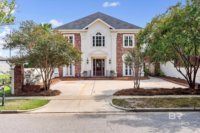 view of front of home featuring brick siding, a shingled roof, and stucco siding