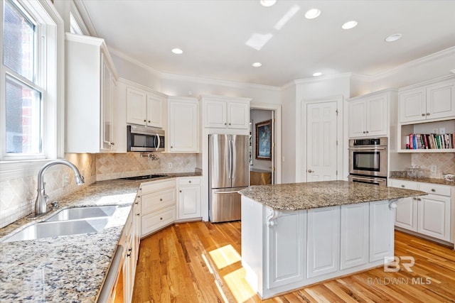 kitchen featuring appliances with stainless steel finishes, ornamental molding, light wood-type flooring, white cabinetry, and a sink