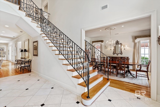 staircase featuring hardwood / wood-style floors, crown molding, and a notable chandelier